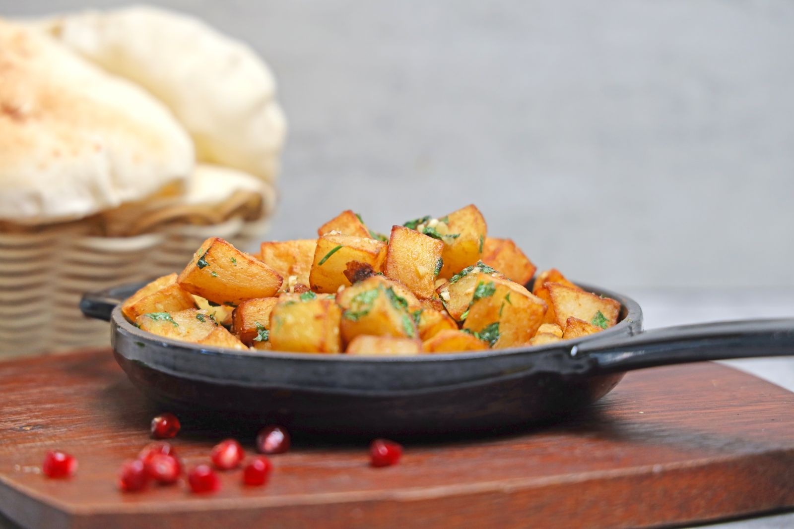 Cubes of spiced fried potato with coriander in a cast-iron pan, flatbread behind